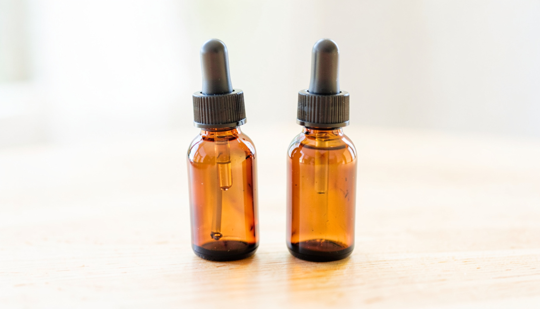 Two small amber glass bottles with droppers on a light wooden table in soft daylight