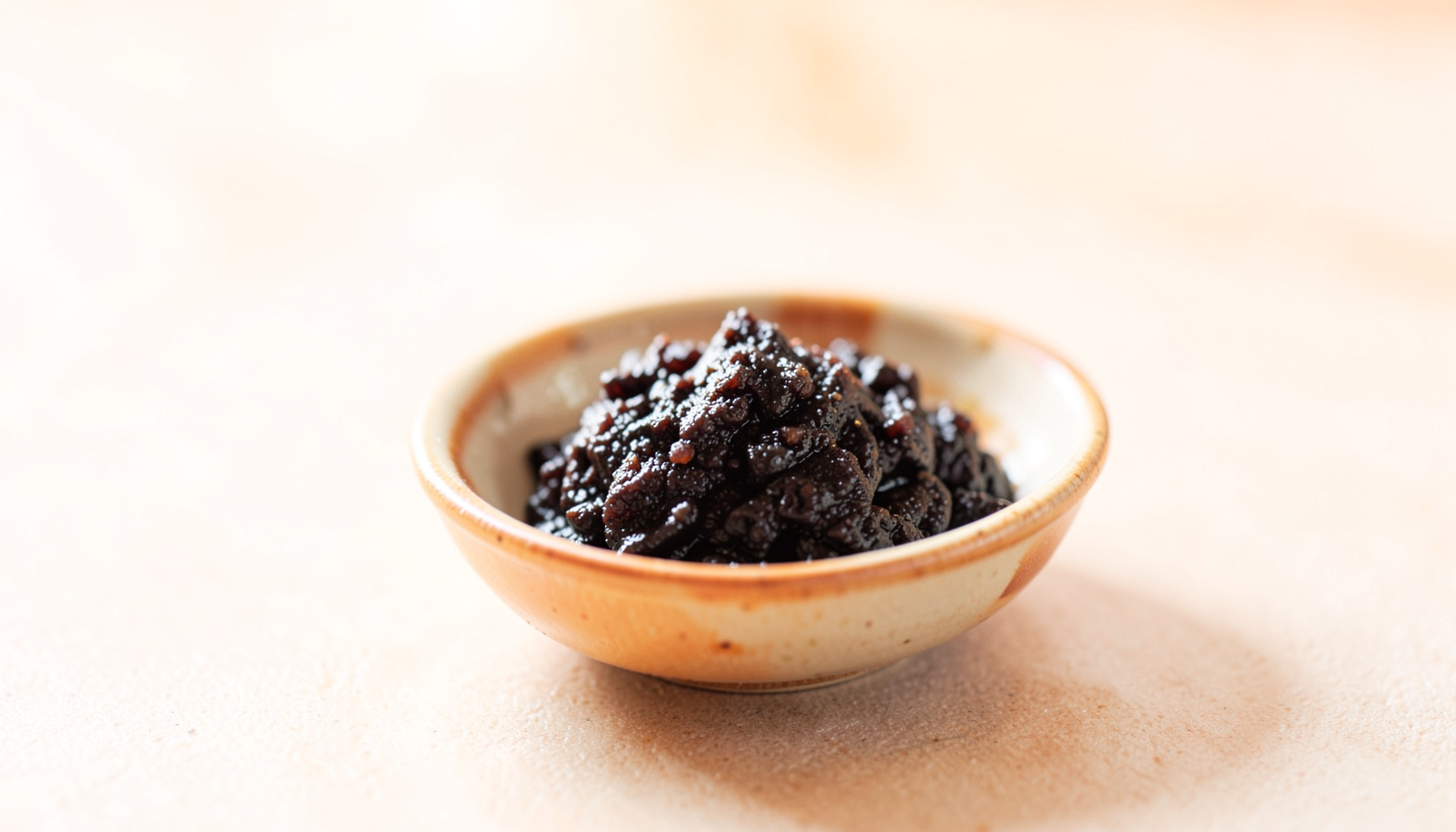 A bright, airy photograph of dark resin-like shilajit paste in a small ceramic dish on a neutral surface, with soft natural daylight and warm earthy tones
