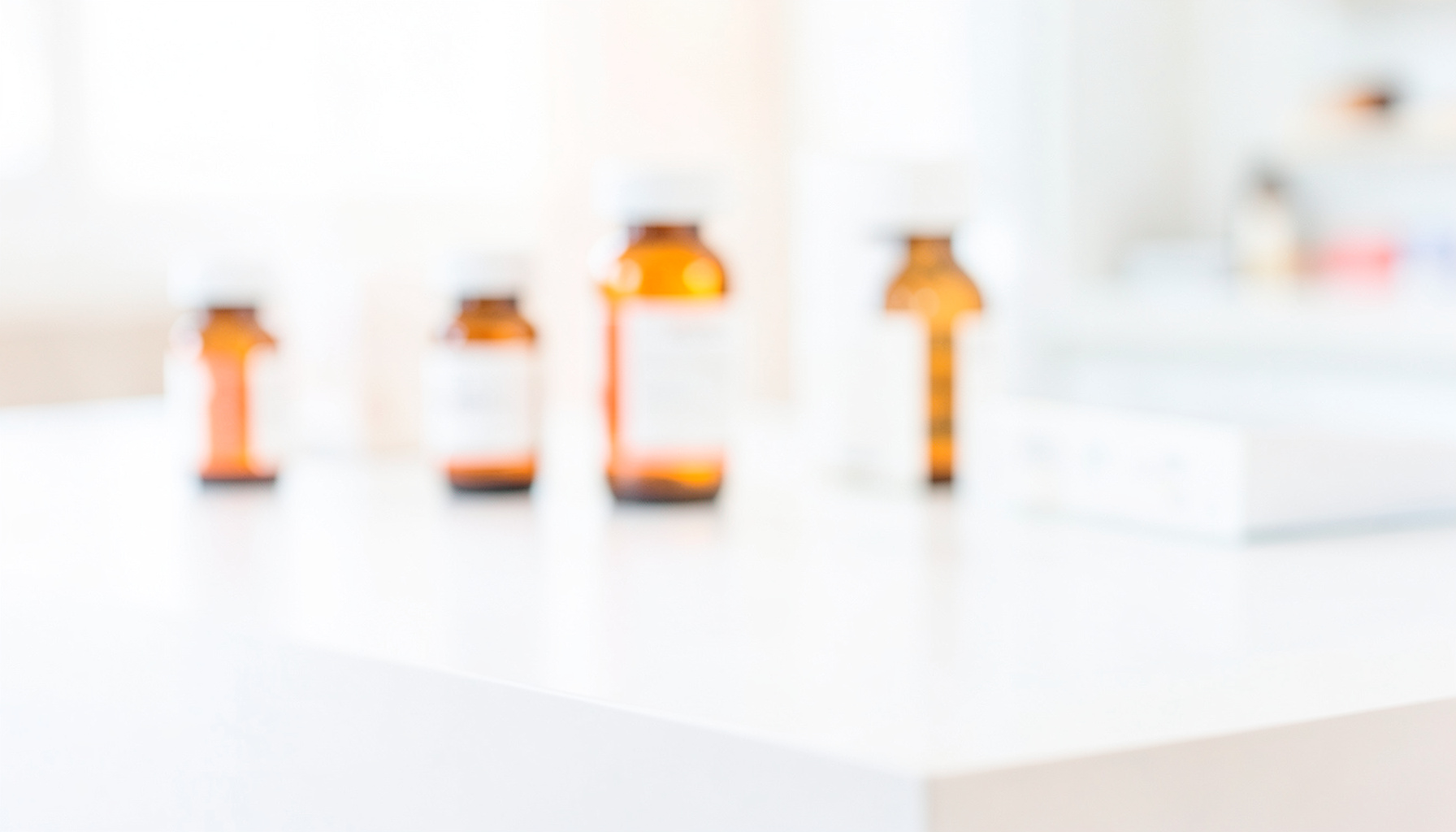 A bright, airy photograph of a clean white pharmacy countertop with a few small amber prescription bottles softly blurred in the background, clinical and professional mood